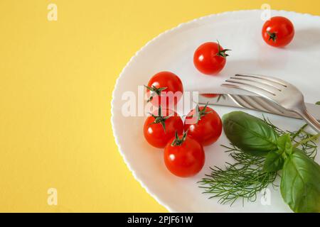 Sur une assiette avec basilic et couverts, faire de la cerise sur le tomate. Alimentation Banque D'Images