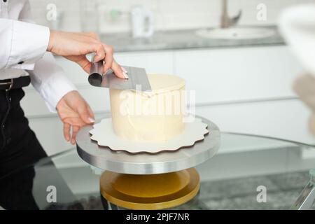 Le confiseur évisse le gâteau, le couvre avec du chocolat blanc. Production à domicile, affaires, entrepreneur, passe-temps. Pâtisseries et bonbons délicieux. Banque D'Images