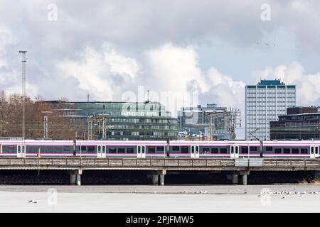 Train de banlieue passant par un pont ferroviaire avec les bâtiments Hakaniemi et Merihaka en arrière-plan lors d'une journée de printemps nuageux à Helsinki, en Finlande Banque D'Images