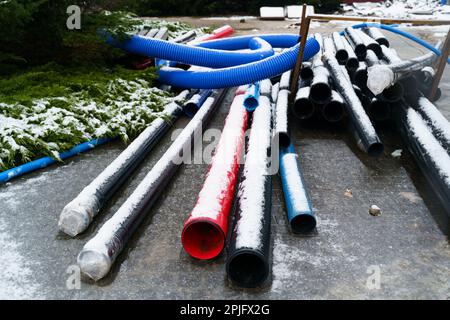 Des pipelines bleus, noirs et rouges de différents diamètres se trouvent sur un chantier de construction en plein air en hiver. Réparation des communications. Banque D'Images