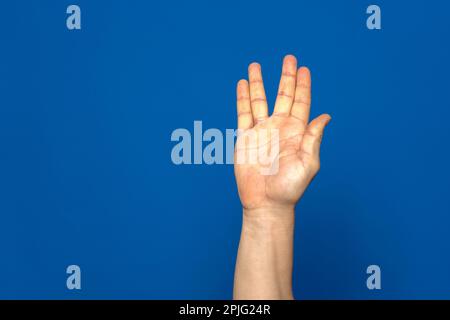 Langue des signes américaine. Main mâle montrant la lettre V faite avec quatre de ses doigts isolés sur fond bleu Banque D'Images