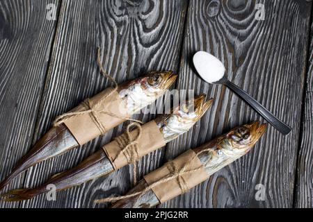 Pupassu fumé froid. Le poisson est enveloppé d'une bande de papier. Noué avec de la ficelle en lin. Repose sur des planches de pin. Cuillère à café avec sel. Gros plan. Banque D'Images