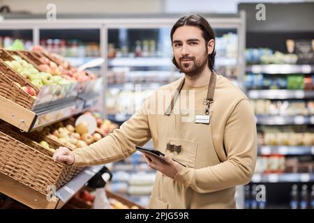 Portrait de l'ouvrier masculin dans un supermarché regardant la caméra tout en se tenant à côté de fruits frais Banque D'Images