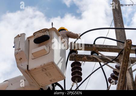 Électricien mâle debout dans le panier de grue mobile et répare un fil de la ligne électrique de puissance sur fond ciel , Thaïlande Banque D'Images