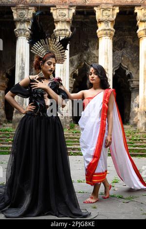 Portrait de deux femmes en saree traditionnel rouge et blanc et en costume d'Halloween, maquillage gothique, debout devant un bâtiment du patrimoine en K Banque D'Images