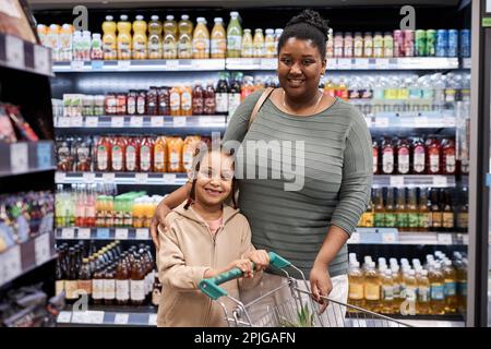 Portrait de la taille de la jeune mère noire avec sa fille dans un supermarché regardant l'appareil photo tout en faisant des courses Banque D'Images