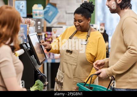 Portrait de femme noire souriante qui aide les clients en caisse libre-service au supermarché Banque D'Images