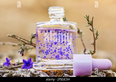 Flacon cosmétique avec sérum pour le visage. Bol en verre avec compte-gouttes. L'huile de cuticule pourpre avec des granulés a un parfum de lavande. Concept de soins de beauté. Anti-âge Banque D'Images