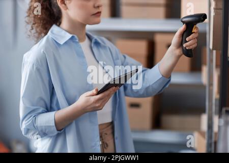 Gros plan d'une jeune femme en chemise bleue lisant les codes qr sur des boîtes emballées avec des articles en ligne commandés sur des étagères dans la salle de stockage Banque D'Images