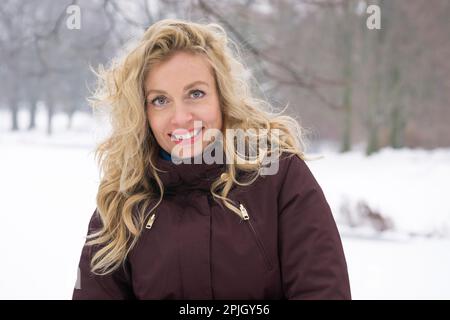 femme blonde qui profite d'une promenade hivernale dans un parc couvert de neige Banque D'Images