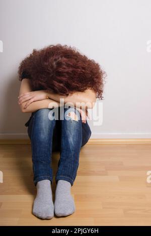 Déprimé triste jeune femme cachant son face sitting on floor Banque D'Images