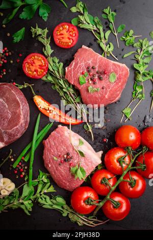 Filet de veau cru sur fond de craie noire avec tomates cerises, poivre chaud et herbes. Prêt à cuire Banque D'Images