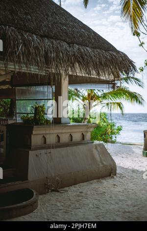 Journée ensoleillée dans un bar de plage de sable construit en grès avec un toit de chaume. Les palmiers à noix de coco avec des feuilles vertes peuvent être vus en arrière-plan, en regardant TH Banque D'Images