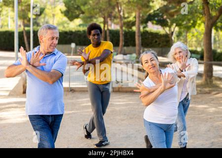 Un entraîneur afro-américain positif aidant les personnes âgées à étirer leurs muscles avant de danser à l'extérieur dans le parc Banque D'Images