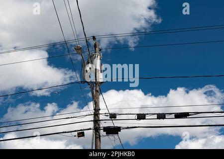 Un poteau utilitaire avec transformateurs et de nombreux câbles et boîtes de communication, lumière de rue LED avec un ciel bleu et un fond de nuage blanc Banque D'Images