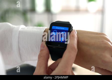 Jeune homme vérifiant la montre-bracelet électronique avec Smart Home interface en intérieur, gros plan Banque D'Images