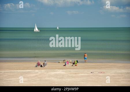 Journée ensoleillée sur la plage de Piriápolis, avec une mer calme et des voiliers à l'horizon. Certaines personnes prennent le soleil sur le sable Banque D'Images