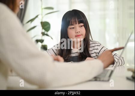 Focalisée petite fille asiatique étudiant l'anglais à la maison avec sa mère, regardant l'écran d'ordinateur portable. tuteur, baby-sitter, enfance Banque D'Images