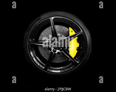 Roue et pneu en alliage de voiture isolés sur fond noir. Nouvelle roue en alliage avec pneu et freins en carbone céramique jaune. Jante en alliage isolée. Disque de roue de voiture. Banque D'Images