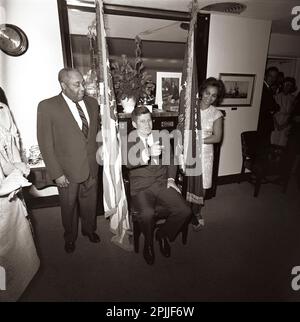 KN-C28776 29 mai 1963 le Président John F. Kennedy assiste à un anniversaire surprise tenu en son honneur par des membres du personnel de la Maison Blanche. Le valet du président Kennedy, George E. Thomas, est à gauche ; une femme non identifiée se trouve à droite. Visible sur la porte tout à droite : Ron Pontius, agent du service secret de la Maison Blanche, Evelyn Lincoln, secrétaire personnel du président Kennedy. Navy Mess Hall, Maison Blanche, Washington, D.C. Veuillez indiquer « Cecil Stoughton ». Photos de la Maison Blanche. John F. Kennedy Library and Museum, Boston Banque D'Images