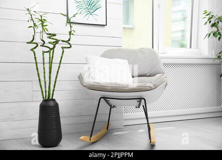 Vase avec tiges en bambou vert et élégant fauteuil à bascule dans la chambre. Design intérieur Banque D'Images