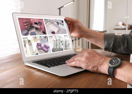 Homme surveillant des caméras CCTV modernes sur une table en bois, en gros plan. Système de sécurité domestique intelligent Banque D'Images