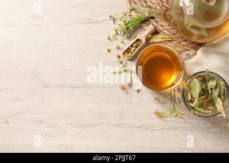 Thé fraîchement infusé et herbes séchées sur table en bois blanc, plat. Espace pour le texte Banque D'Images