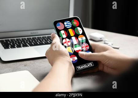 Traducteur utilisant un smartphone avec des images de différents drapeaux sur l'écran à la table, gros plan Banque D'Images