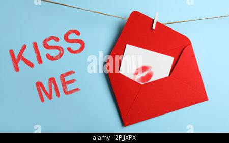 Carte avec imprimé à lèvres dans une enveloppe rouge et l'expression Kiss Me sur fond bleu clair Banque D'Images