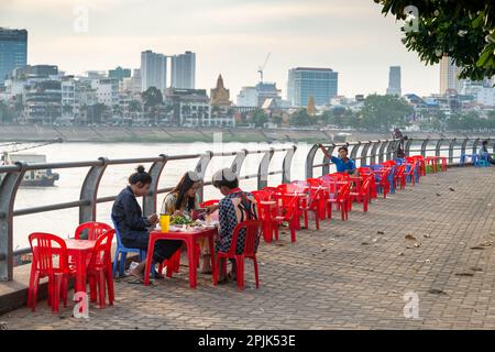 Phnom Penh,Cambodge-24 décembre 2022:adolescents Khmers, s'asseoir à une petite table, sur de petites chaises en plastique, dîner au coucher du soleil, le long de beaucoup moins de develo Banque D'Images