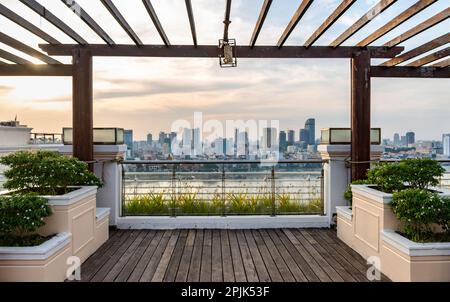 Phnom Penh,Cambodge-24 décembre 2022:encadré par des poutres en bois d'un grand balcon, avec des plantes décoratives et des terrasses en bois, le coucher du soleil se trouve au-dessus Banque D'Images