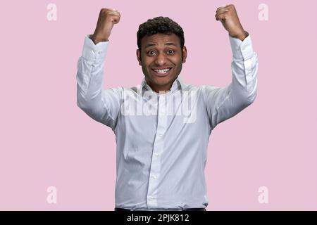 Un homme indien ou arabe enthousiaste et émerveillé se réjouit du succès. Concept de victoire et de victoire. Arrière-plan rose isolé. Banque D'Images