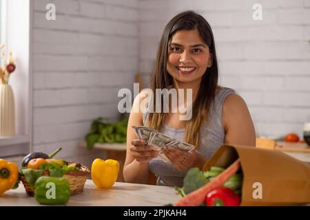 Femme comptant de l'argent dans la cuisine après avoir fait du shopping Banque D'Images