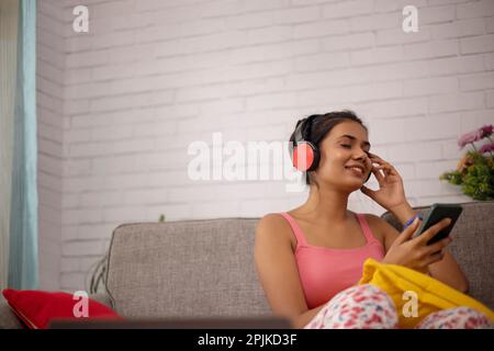 Une jeune femme écoute de la musique à l'aide d'un casque tout en se détendant sur un canapé à la maison Banque D'Images