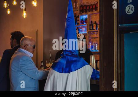Séville, Espagne; 2 avril 2023:Nazaréen achetant de la nourriture dans un bar le dimanche des palmiers. Confrérie de la Hiniesta. Banque D'Images