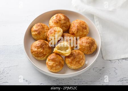 Profiteroles au fromage, gougres, pâtisseries françaises traditionnelles, dans une assiette blanche sur fond gris clair, vue du dessus Banque D'Images