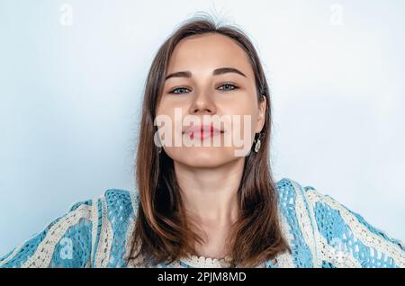 Femme souriante aux cheveux sombres regardant l'appareil photo. Chemisier en dentelle bleue. Arrière-plan blanc Banque D'Images