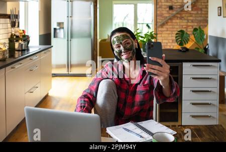 Gros plan d'une jeune femme adulte prenant un selfie alors qu'elle travaille à la maison sur son ordinateur portable Banque D'Images