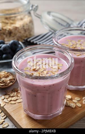 Verres de délicieux smoothie aux myrtilles avec flocons d'avoine sur panneau de bois, gros plan Banque D'Images