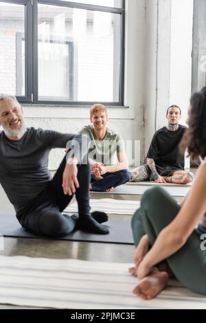 Des hommes gais parlant à une femme floue sur le tapis dans la classe de yoga, image de stock Banque D'Images