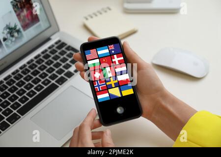 Traducteur utilisant un smartphone avec des images de différents drapeaux sur l'écran à la table, gros plan Banque D'Images