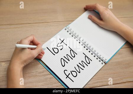 Femme écrivant phrase perdue et trouvée dans le carnet à table en bois, gros plan Banque D'Images