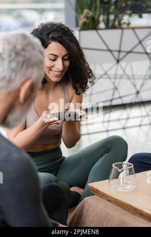 bonne femme du moyen-orient regardant l'assiette avec le thé comprimé de puer près de l'homme d'âge moyen sur le premier plan flou, image de stock Banque D'Images