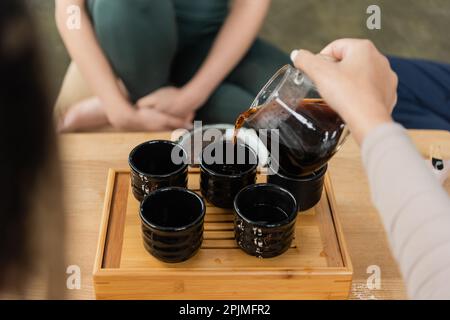 vue rognée de la femme qui verse le puer de la verseuse en verre dans les tasses à thé traditionnelles, image de stock Banque D'Images