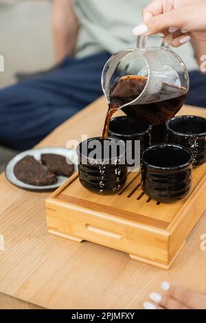 vue rognée de la femme qui verse le puer filtre de la verseuse en verre dans les tasses à thé traditionnelles, image de stock Banque D'Images