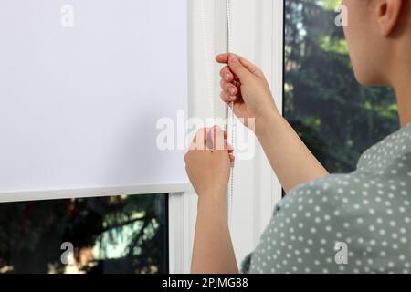 Femme ouvrant le store blanc sur la fenêtre à l'intérieur, gros plan Banque D'Images