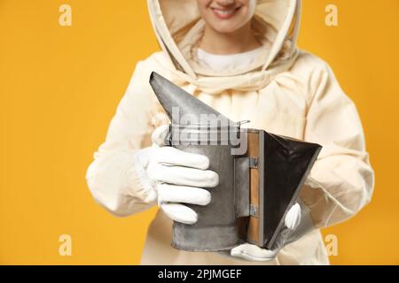 Apiculteur en uniforme tenant le pot de fumée sur fond jaune, gros plan Banque D'Images