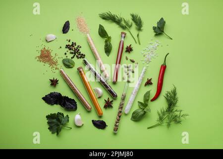 Composition de la couche plate avec différentes épices, tubes à essai et herbes fraîches sur fond vert Banque D'Images