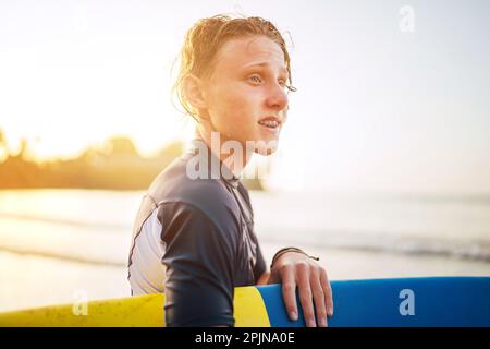 Portrait d'un jeune garçon avec des bretelles dentaires et des cheveux mouillés avec une planche de surf va pour le surf. Il sourit et marche dans l'eau. Bonne enfance et Banque D'Images