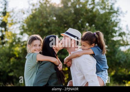 Portrait de jeune couple avec leurs filles dans la nature, embrassant. Vue latérale. Banque D'Images